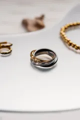 Anillo de acero quirúrgico con tres aros entrelazados, uno dorado, uno plateado y uno negro.