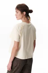 Remera blanca de manga corta con detalle de encaje floral en el hombro.