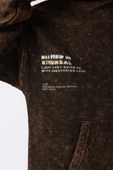 Buzo canguro negro con capucha, de corte oversize y estética lavada. Presenta un bolsillo tipo canguro y puños con orificio para el pulgar. Estampado con texto en el lateral izquierdo.