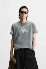 Camiseta gris con efecto lavado, corte relaxed fit, cuello redondo y manga corta. Estampado frontal de una mosca en color blanco.