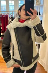 Campera gamulán marrón con interior de piel sintética color crema, cierre frontal con cremallera y bolsillos laterales con cremallera.