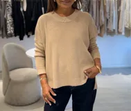 Sweater color beige con cuello redondo y mangas largas. Tejido de punto con hilado metalizado. Delantera más corta que la parte trasera, con aberturas en los laterales.