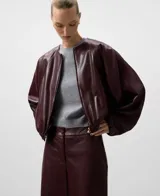 Chaqueta bomber de piel sintética color burdeos, con cuello redondo, manga japonesa ancha con puño elástico y bajo elástico. Cierre frontal con cremallera.