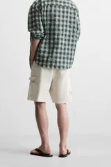 Bermuda color verde militar, de corte relaxed fit, con bolsillos frontales y traseros tipo plaqué, detalle de tira y bolsillo multifunción en la pierna, y bajo irregular.