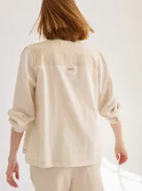 Camisa color crudo de corte recto y manga larga, con cuello mao y botones de madera. Presenta detalles de bordado calado en el frente.