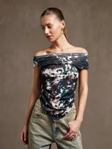 Top negro con estampado abstracto en blanco y rosa, escote off-shoulder y corte irregular.