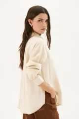 Camisa beige de corte recto, con cuello clásico, cierre frontal con botones, bolsillo en el pecho y mangas largas con puños abotonados.