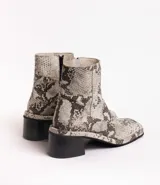 Botas cortas de cuero con estampado de piel de serpiente en tonos grises y negros. Tienen un tacón bloque de madera negro y cierre lateral con cremallera.