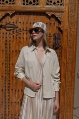 Camisa blanca de lino con bordados dorados de árboles, corte recto, cuello camisero y mangas largas con puños abotonados.