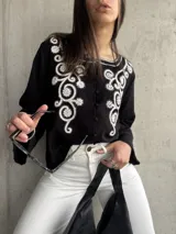 Camisa negra de manga ancha con bordado floral blanco en el frente y cierre con botones.