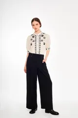 Pantalón negro de corte palazzo con cintura alta y detalle de ojales metálicos con cordones cruzados.