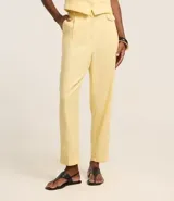 Pantalón zanahoria de cintura alta color amarillo pastel, confeccionado en viscolino con 15% de lino, con trabillas en la cintura, solapas con botón abajo de la cintura, pliegues y cierre tradicional.
