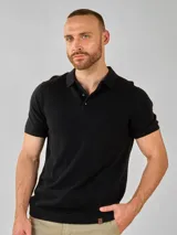 Remera de punto color negro, manga corta, con cuello polo y botones en la abertura frontal. Presenta un tejido texturizado y un dobladillo acanalado.