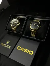 Conjunto de dos relojes: uno marca Rolex dorado con esfera negra y bisel giratorio, y otro marca Casio negro con detalles dorados y esfera cuadrada.