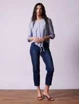 Blusa de algodón a rayas verticales azules y blancas, con cuello en V, mangas 3/4 y cierre frontal con botones. Tiene un nudo en la parte delantera.