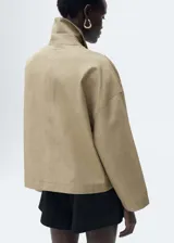 Chaqueta color beige de corte recto con cuello camisero, cierre frontal con botones y mangas largas.