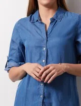 Camisa celeste de tencel con cuello con solapa, escote en V, abertura central con botones y mangas 3/4 regulables con presilla y botón.