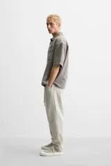 Pantalón color arena de corte recto, confeccionado en tejido de algodón y lino. Cuenta con cintura elástica ajustable con cordón, bolsillos delanteros y traseros de parche.