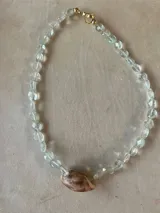 Collar largo de cuentas de piedras semipreciosas en tonos tierra, con dijes de conchas marinas.