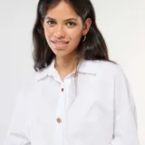 Camisa blanca de corte oversize, con cuello clásico, mangas largas y cierre frontal con botones fantasía dorados.