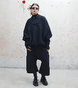 Buzo negro oversize con cuello alto, mangas largas abullonadas y puños ajustados. Pantalón negro tipo babucha con corte ancho y botas negras de plataforma. Incluye collar plateado y lentes de sol.