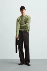 Sweater verde claro de punto con cuello redondo y mangas largas. Presenta diseño de trenzas en el centro y en las mangas.