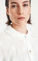 Camisa blanca con bordado de flores blancas, de manga corta y corte recto.