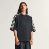 Camiseta negra de corte oversize con cuello en V ribeteado en blanco. Presenta las tres franjas blancas en las mangas raglán y el logo adidas en relieve en el pecho.