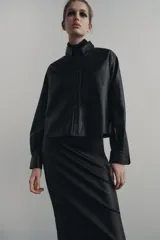 Sobrecamisa negra de efecto piel, con cuello de solapa, manga larga con puños abotonados, bajo recto y cierre frontal con botones.