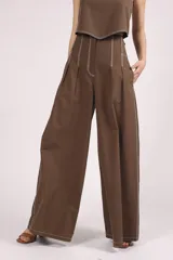 Pantalón negro de tiro alto, corte ancho y largo, con pliegues frontales y pespuntes contrastantes en blanco en la cintura y bolsillos.