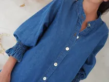 Vestido camisero corto de denim celeste, con cuello mao, mangas 3/4 con elástico en los puños y cierre frontal con botones de nácar.