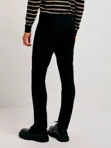 Pantalón de jean negro, corte ajustado (skinny), con tiro medio y cierre de botón y cremallera.