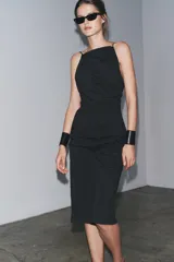 Vestido midi negro de tirantes finos, con cuello halter, detalle de drapeado y cierre con cremallera oculta.