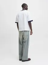 Remera blanca de manga corta y cuello redondo, con fit oversize y largo cropped. Tiene ribetes azul marino en el cuello y las mangas. Estampado frontal con la palabra "ORIGINALS" en negro y "studio" en cursiva, junto a detalles en rojo como "1990" y "COPENHAGEN CREATIVE DEPT.".