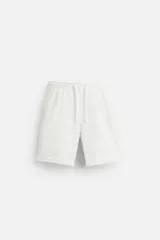 Bermuda blanca de cintura elástica ajustable con cordón, detalle de pliegues frontales, bolsillos delanteros y traseros de vivo. Bajo con vuelta.