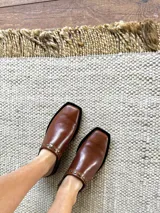 Mules de cuero color marrón con punta cuadrada y detalle de tachas doradas.
