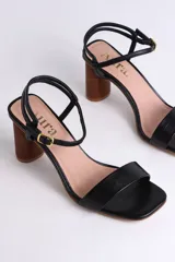 Sandalias de cuero negro con tacón cilíndrico de madera y tira fina con hebilla al tobillo.
