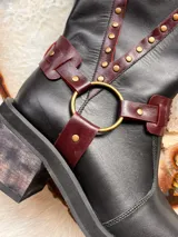 Botas de cuero negro con detalles en color borgoña, hebilla en la parte superior y arnés con aro metálico.