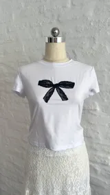 Remera blanca ajustada al cuerpo con estampado de moño de encaje negro en el centro.