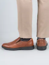 Zapato slip-on de cuero color marrón con suela negra y elástico lateral.