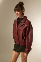 Campera estilo biker de eco-cuero color bordó, con cuello solapa ancho, manga larga y calce holgado. Presenta cierre frontal y botones decorativos en la parte inferior delantera.