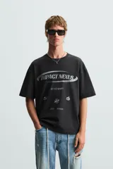 Camiseta negra de corte relaxed fit, cuello redondo y manga corta. Estampado frontal con la frase "Impact Nexus" y otros logos pequeños.