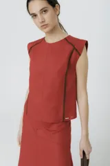 Blusa color ladrillo de lino 100% con cuello redondo y sin mangas. Presenta vivos y pespuntes a contratono en color marrón.