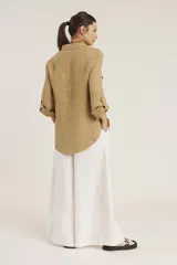 Camisa de lino color beige con cuello clásico, cierre frontal con botones, mangas largas con trabillas para enrollar y dos bolsillos con solapa en el pecho.