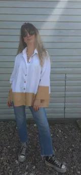 Camisa blanca de lino con mangas largas y corte holgado. Presenta un bloque de color marrón en la parte inferior.