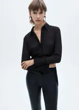 Camisa negra de plumeti con cuello camisero, manga larga con puños abotonados y cierre frontal de botones oculto.