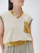 Chaleco de punto color crudo con cuello en V y bolsillo de parche con estampado floral en tonos amarillos y verdes.