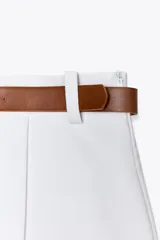 Falda pantalón blanca de tiro alto con cinturón marrón y delantero cruzado. Cierre lateral con cremallera oculta.