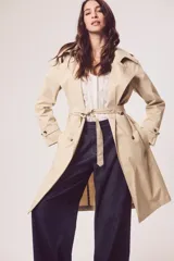 Trench color beige con doble botonadura, cinturón y cuello clásico.