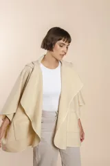 Ruana color crudo de lana fina sin teñir, con capucha, bolsillos y terminaciones envivadas. Tiene un broche para usar cerrada. Es una prenda oversize sin forro, cómoda, versátil y fácil de combinar.